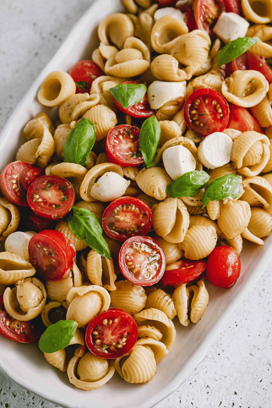 Frischer Nudelsalat Caprese mit Cherrytomaten, Mini Mozzarella und Basilikum in einer Schüssel.