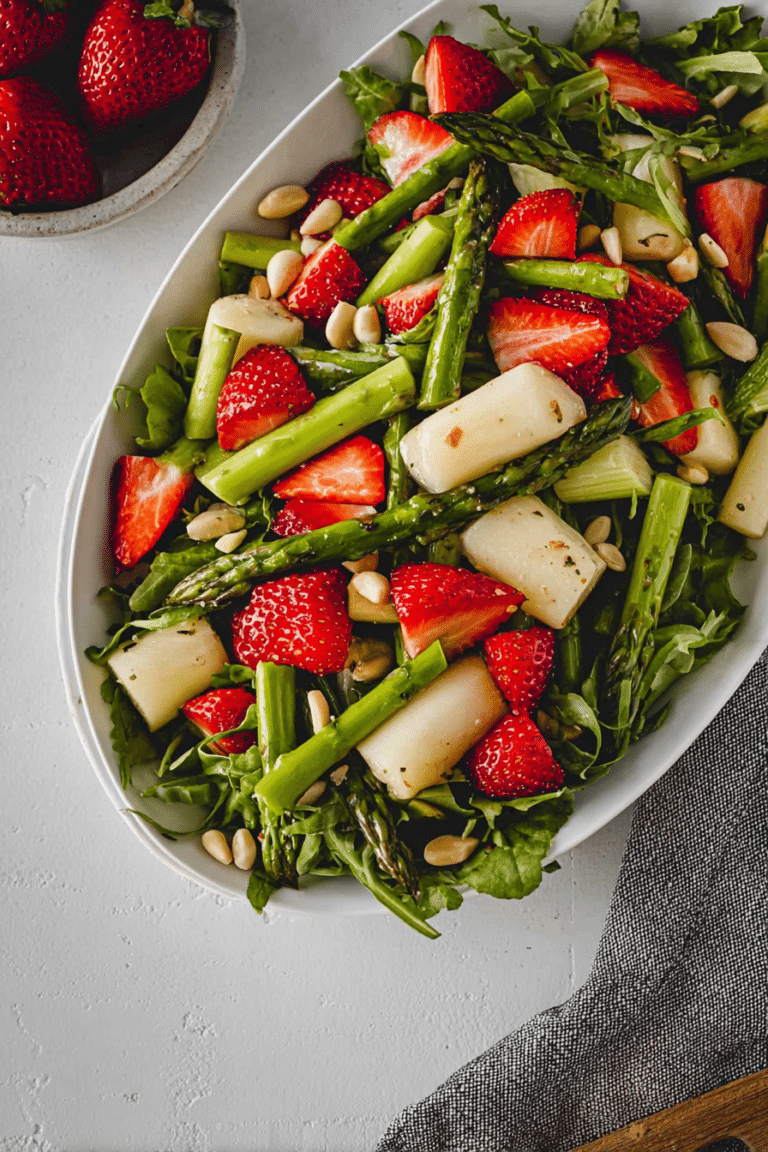 Bunter Spargelsalat mit Erdbeeren, Rucola und Pinienkernen auf einem Tisch, bereit zum Servieren.