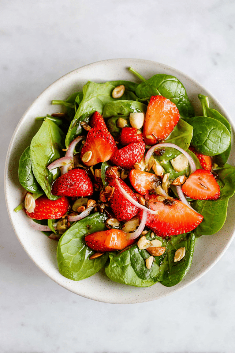 Spinatsalat mit Erdbeeren und Avocado auf einem Holzbrett serviert, umgeben von frischen Zutaten.