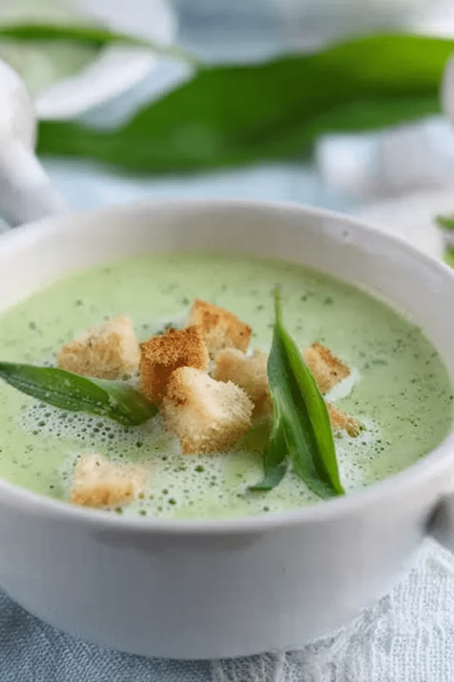 Bärlauchschaumsuppe mit Croutons serviert in einer Schüssel, umgeben von frischem Bärlauch und Brot.