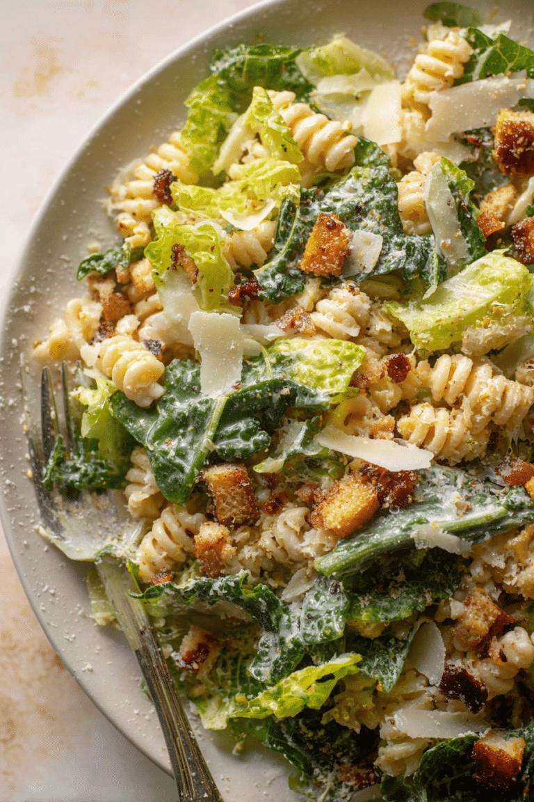 Leckerer Caesar Pasta Salat mit frischem Römersalat, knusprigen Croutons und geriebenem Parmesan auf einem Holztisch.