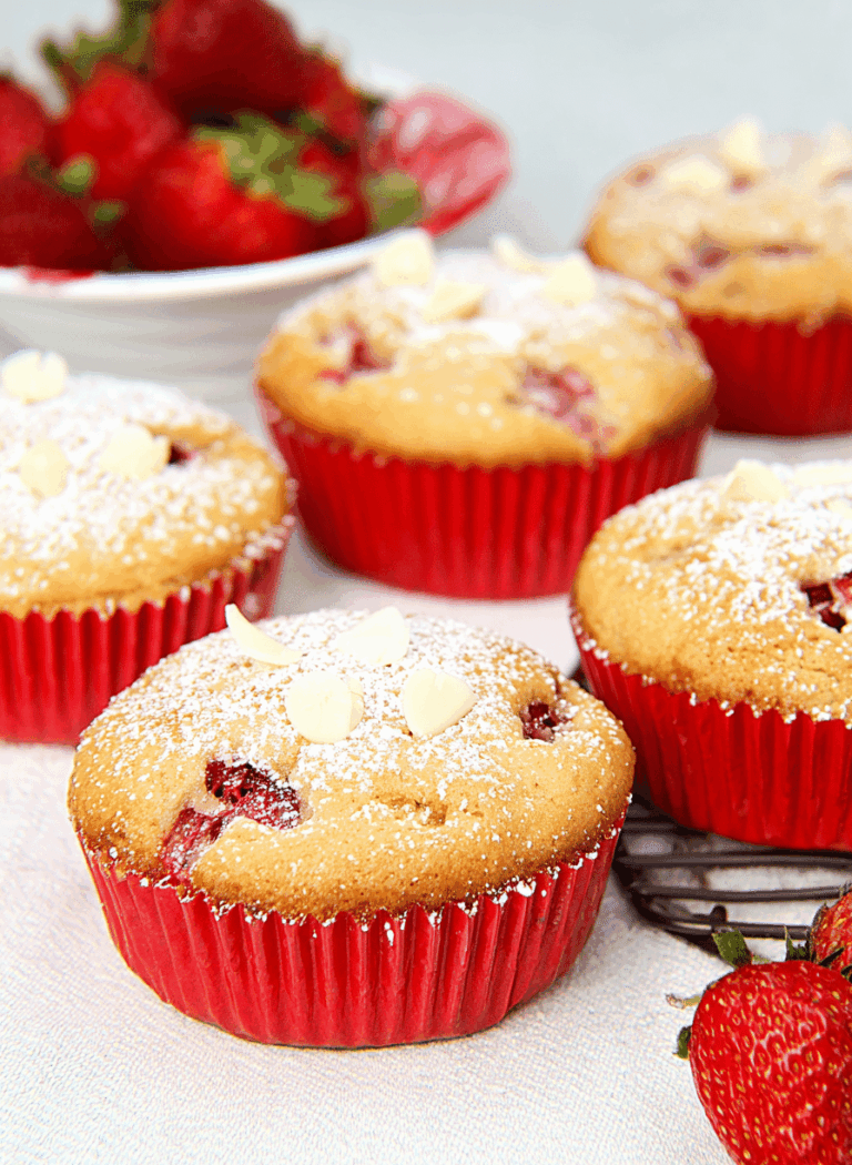 Leckere Erdbeer Muffins mit weißer Schokolade auf einem Holzbrett, dekoriert mit frischen Erdbeeren und Puderzucker.