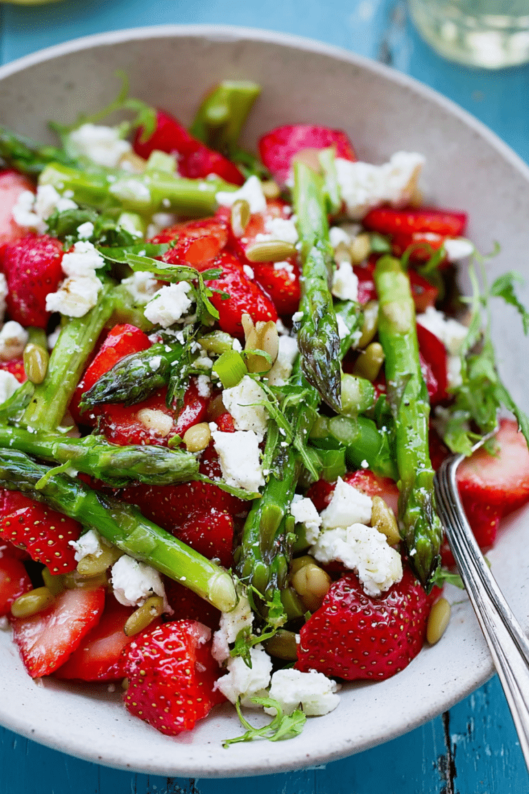Erdbeer-Spargel-Salat mit Feta und Pinienkernen in einer Schüssel, umgeben von frischem Obst und Gemüse.