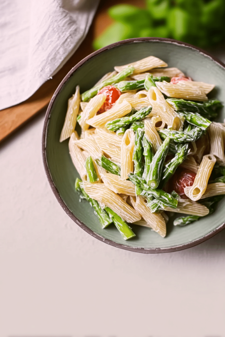 Grüne Spargel Pasta in einer Schüssel, garniert mit Parmesan und Pfeffer, umgeben von frischen Zutaten.