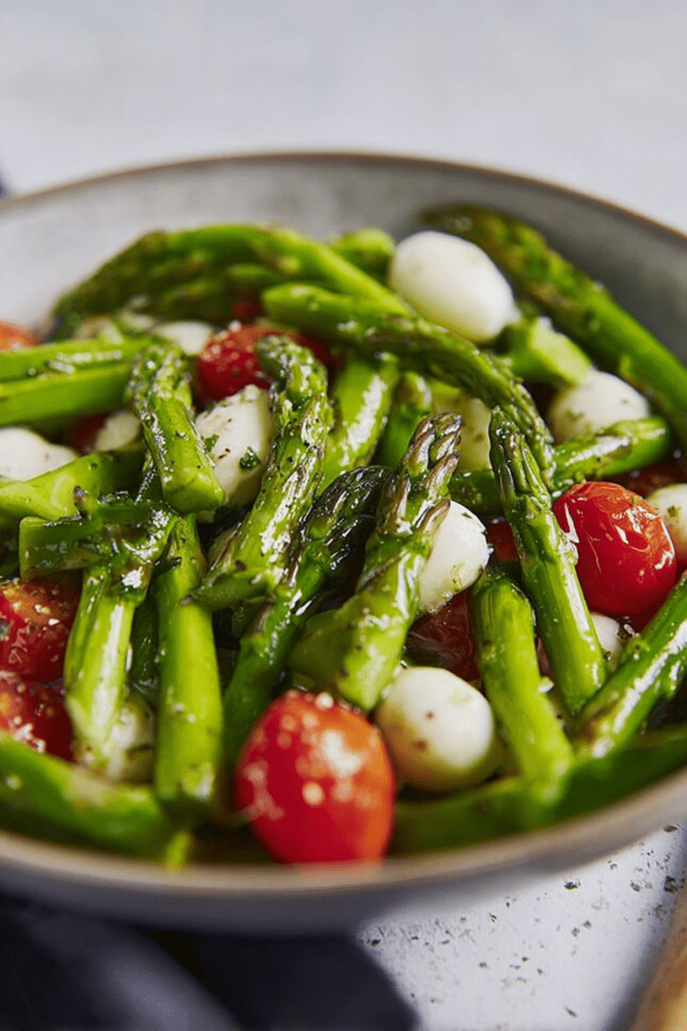 Grüner Spargel Salat mit Kirschtomaten und Mozzarella in einer Schüssel, dekoriert mit frischen Kräutern.