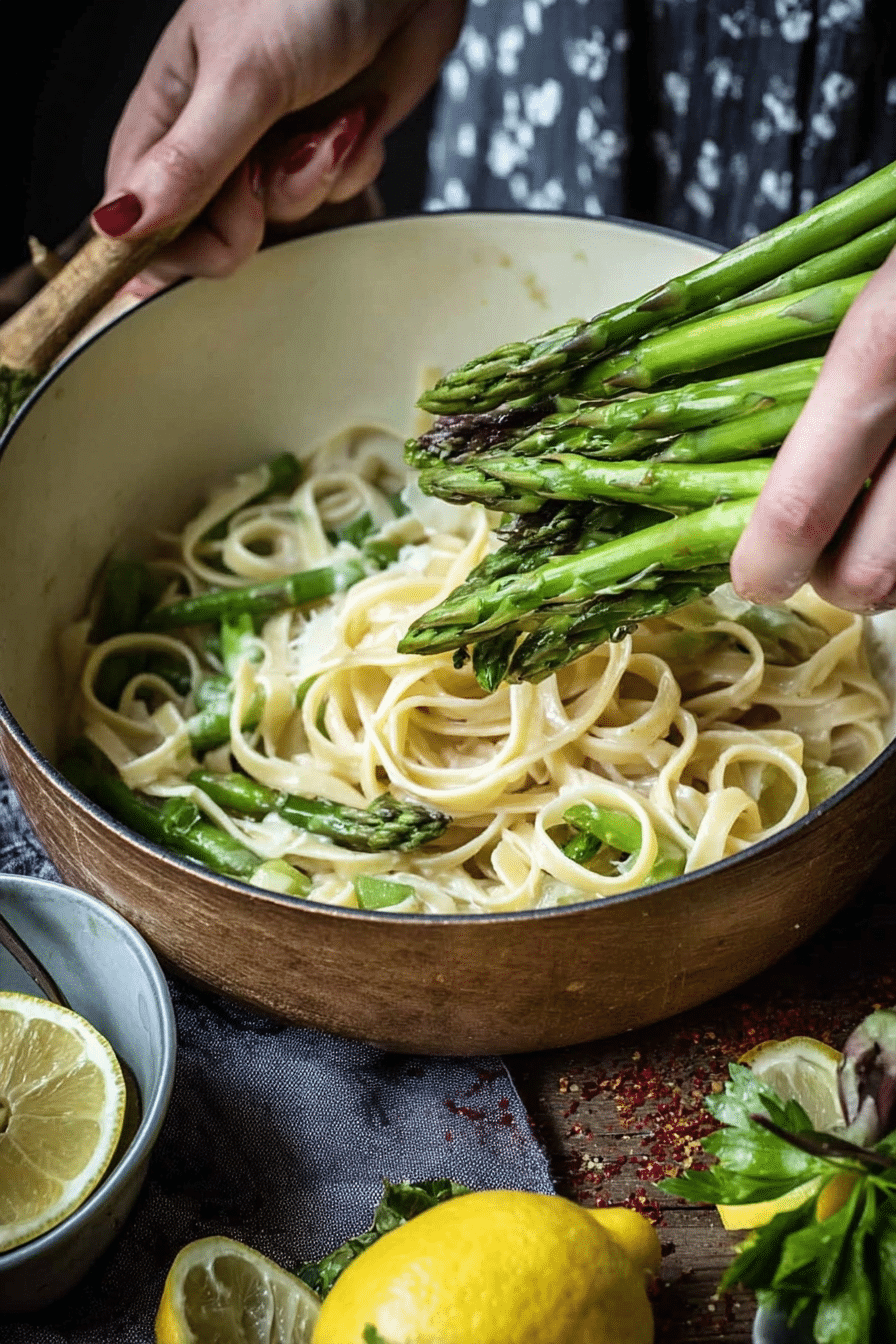 Zitronen Pasta mit grünem Spargel und Parmesan auf einem Teller. Frische Basilikumblätter und Zitronenscheiben dekorieren das Gericht.