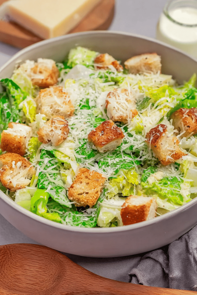 Frisch zubereiteter Caesar Salad mit Croûtons und Parmesan auf rustikalem Holztisch.