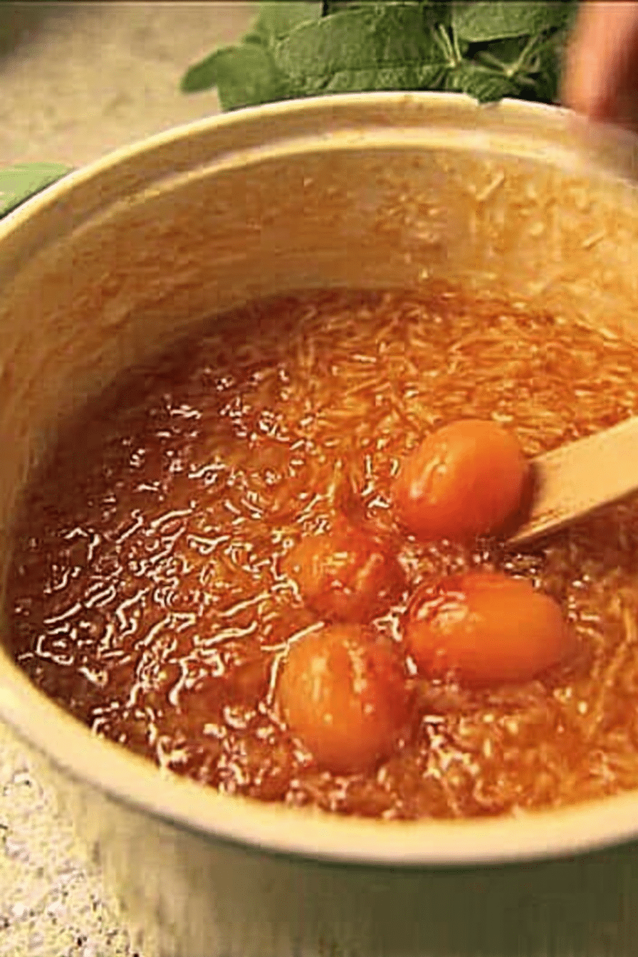 Selbstgemachtes Marillenchutney in einem Glas mit frischen Marillen, Zwiebeln und Gewürzen auf einem rustikalen Tisch.