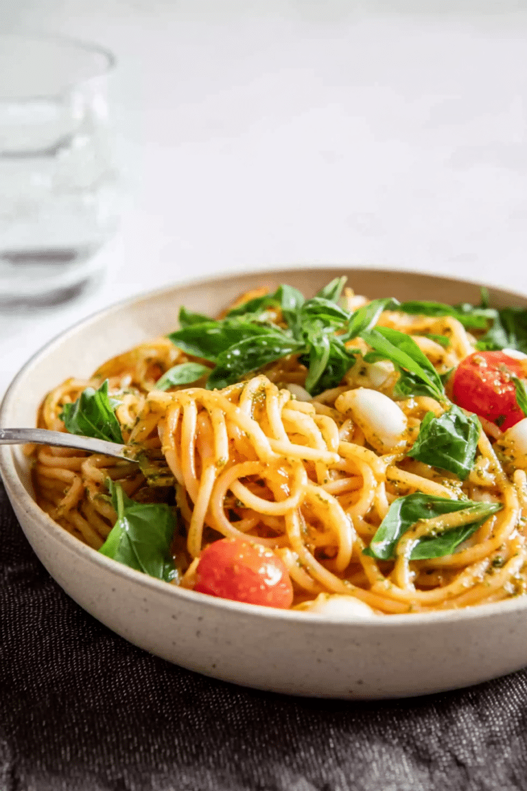 Spaghettisalat mit Pesto, Rucola, kleinen Tomaten und Mozzarella in einer bunten Schüssel.