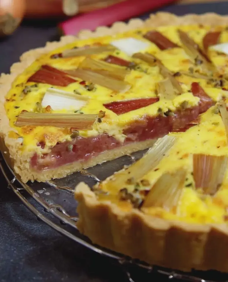Frisch gebackene Spargel-Rhabarber-Quiche auf einem Esstisch mit frischen Spargel- und Rhabarberständen.