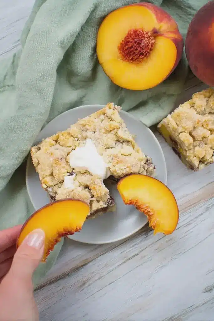 Veganer Pfirsich-Streuselkuchen mit frischen Pfirsichen und Streuseln auf einem Holzbrett.