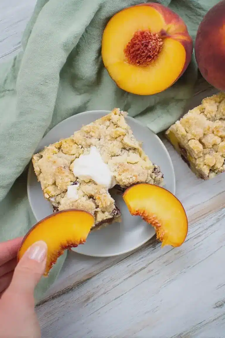 Veganer Pfirsich-Streuselkuchen mit frischen Pfirsichen und Streuseln auf einem Holzbrett.